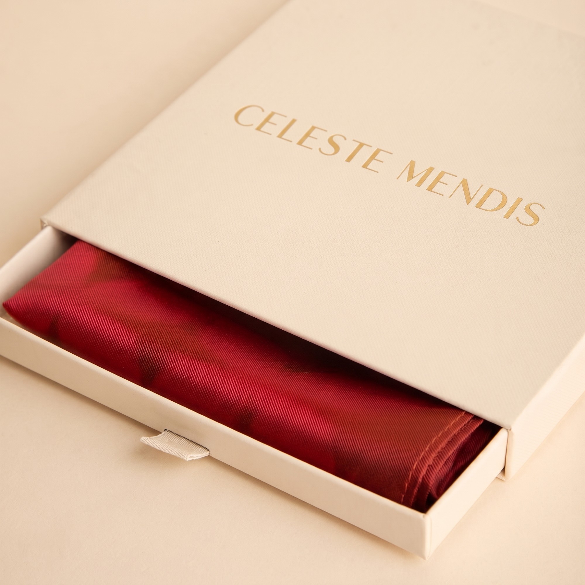 Cream CELESTE MENDIS slide box with gold-foil wordmark, opened to reveal a folded red silk scarf
