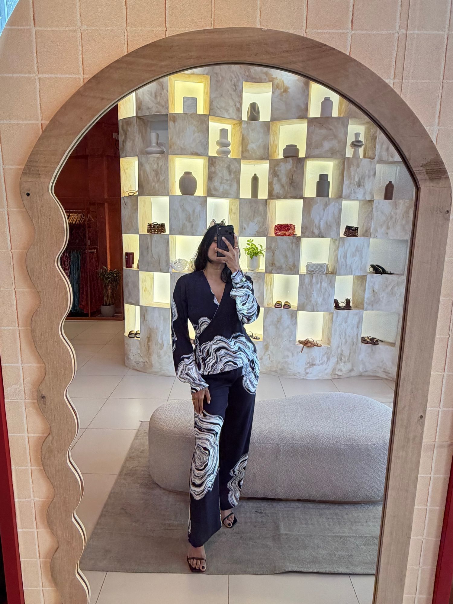 Mirror view of the store: lit checkerboard display niches with vases, bags and shoes, and a Celeste Mendis printed wrap set